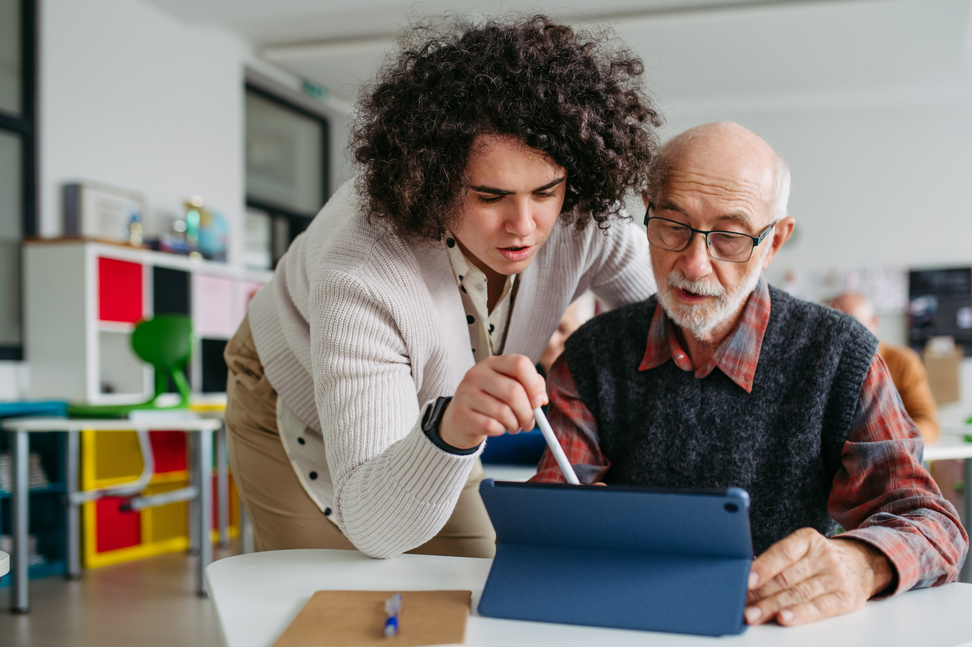 Een vrijwilliger helpt een jongere in een rolstoel met een tablet